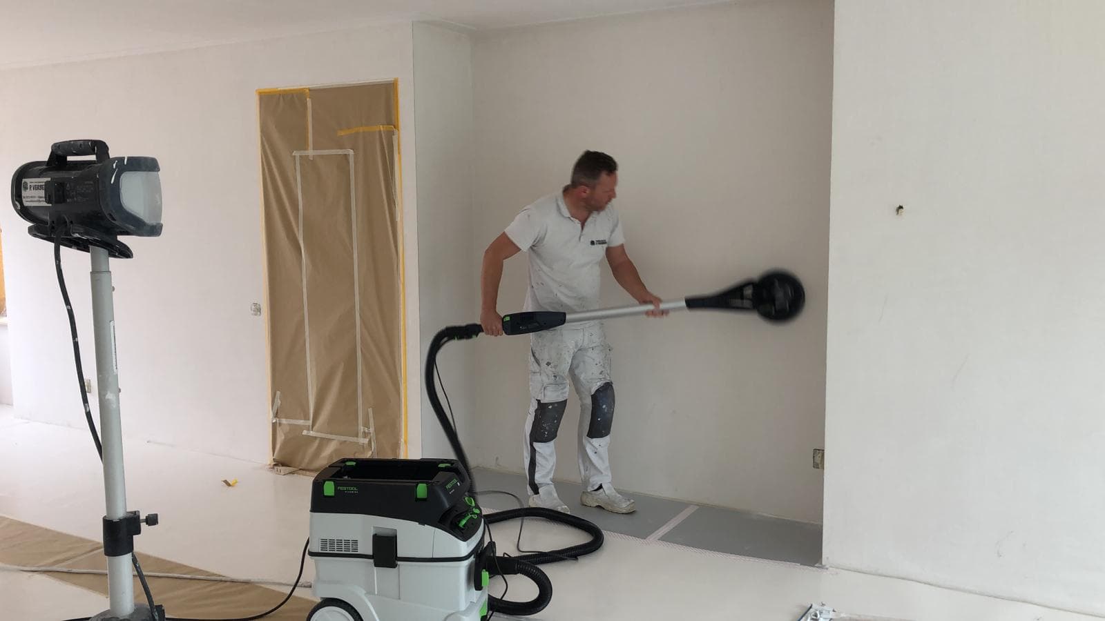 Schilder van P. Verberg schuurt een wand stofvrij met professionele apparatuur