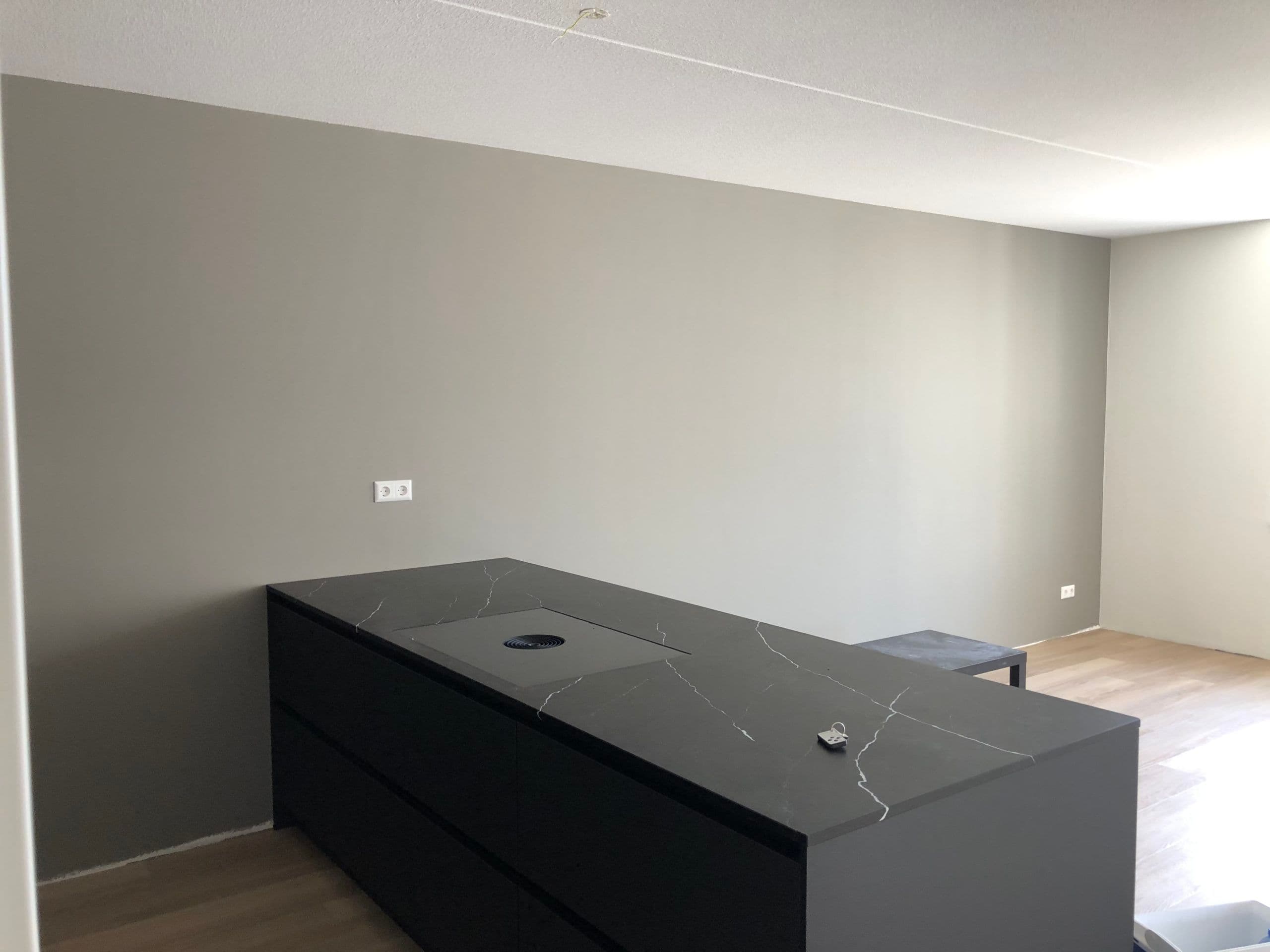 Strak afgewerkte grijze accentmuur in een keuken na behandeling door P. Verberg